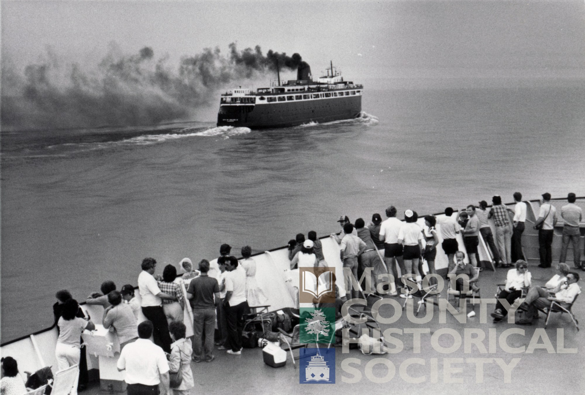 P1855 Photo taken from Badger – City of Midland in background WATERMARKED a group of people in a boat on a body of water