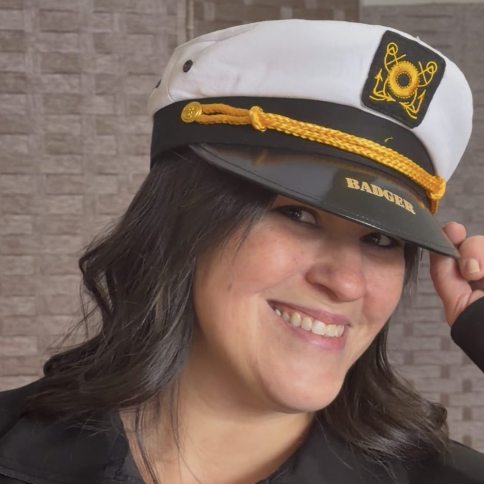 Smiling woman in a captain's hat with badge, tilting it slightly.