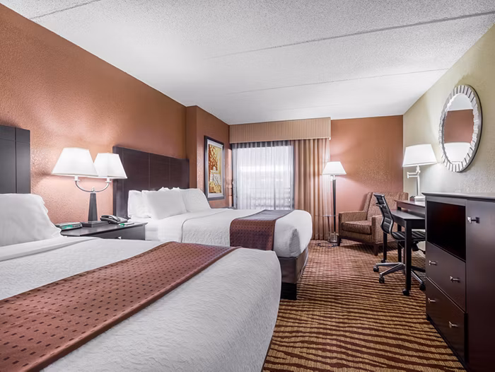 Hotel room with two beds, desk, chair, and lamps.