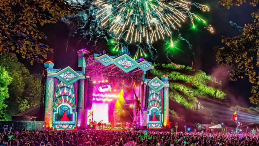 Colorful fireworks above a brightly lit concert stage at night, crowd watching.