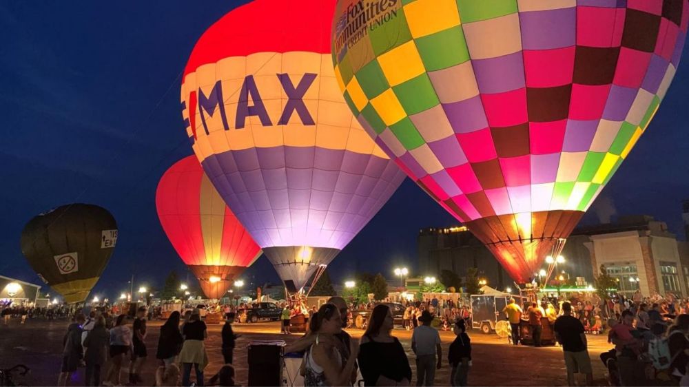 Colorful hot air balloons illuminated at night, with people gathered around.