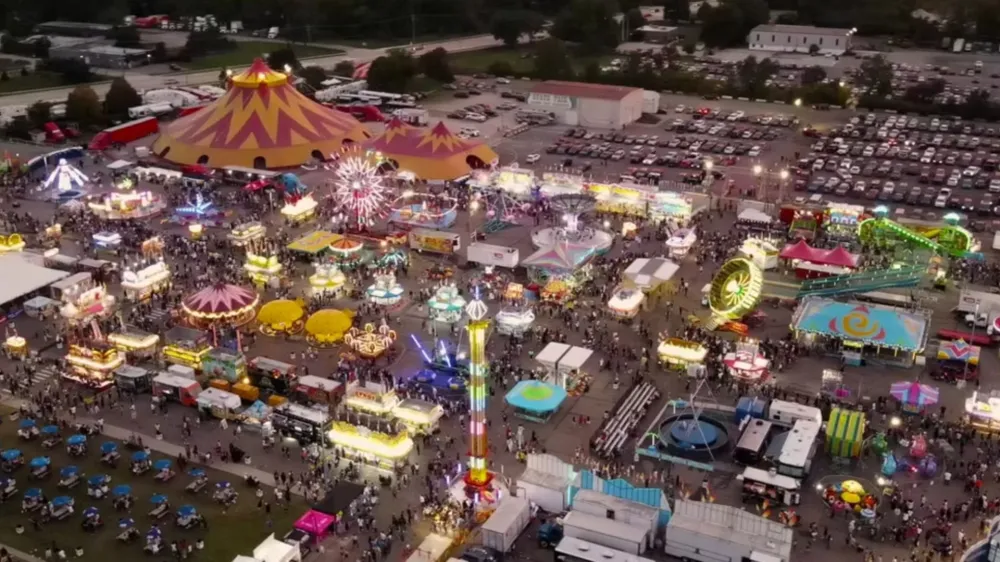 Aerial view of a bustling fairground with rides, tents, and attractions at dusk.