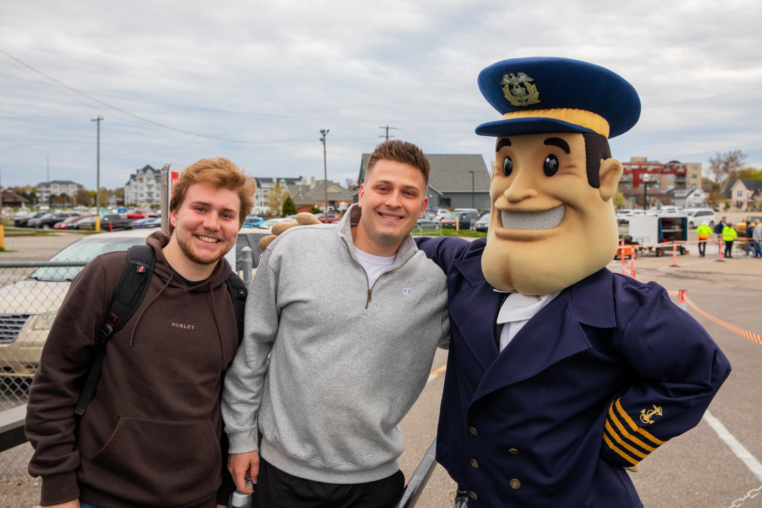 Two men smiling with a person in a blue mascot costume outdoors.