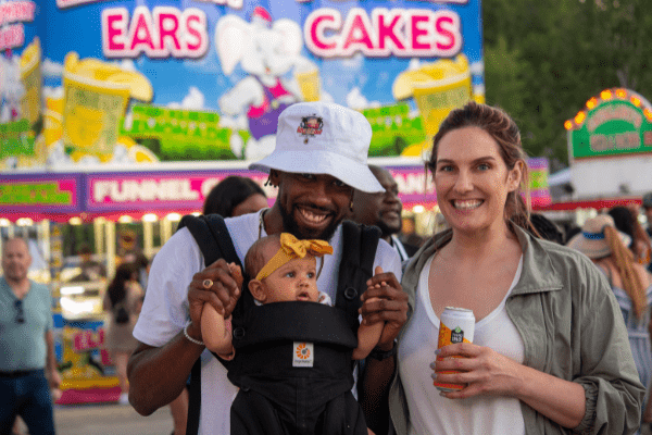 Smiling couple with baby in front of carnival stand.