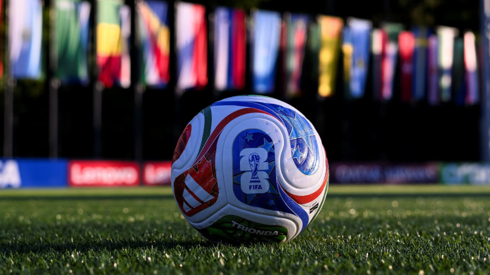 Soccer ball on grass with colorful flags in the background.