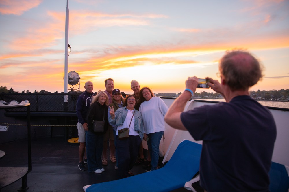 Group poses for a photo on a boat at sunset.