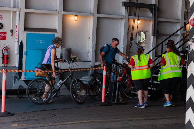 People with bicycles interacting with workers in safety vests on a ferry.