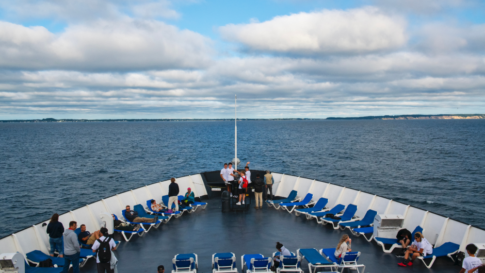 People on a ship deck with blue lounge chairs overlooking the sea.